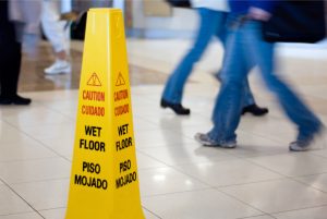 Caution,Wet,Floor,Sign,With,People,Walking,In,The,Background